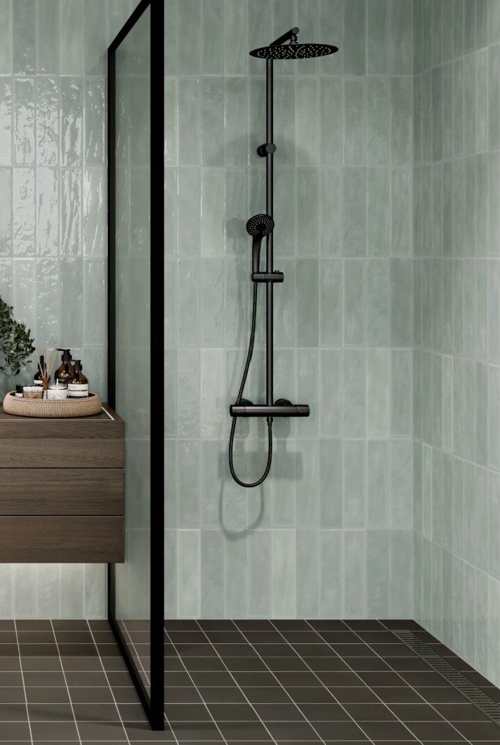 Reference photo of sage green glazed vertical tile in a shower with black fixtures